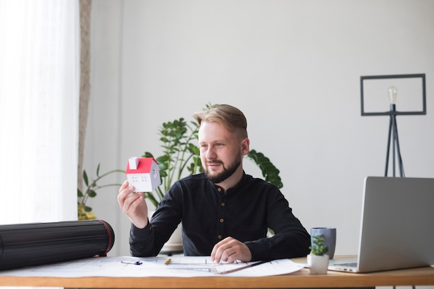 Portrait of a young male architecture holding house model while sitting in office