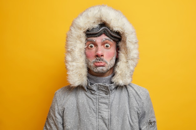 Free photo puzzled frozen young man covered with snow spends all day outdoor during cold frosty weather low temperature being active skier dressed in warm jacket.