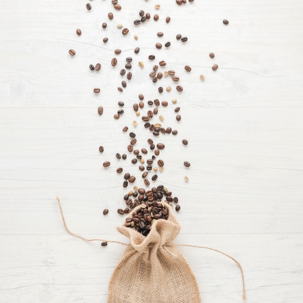 Free photo raw and roasted coffee beans falling from small sack on desk