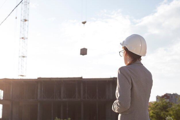 Rear view of female architect wearing hart hat looking at construction site