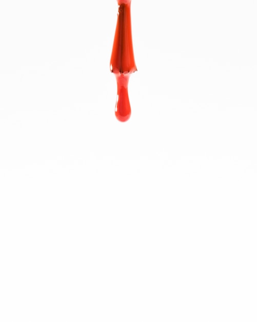 Free photo red drop of nail polish and brush isolated on white backdrop