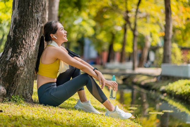 Free photo relax casual asian female sportwoman break time after finish morning run exercise healthy lifestyle asian female relax cooling down after run training under the tree near water in the park