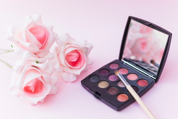 Free Photo roses with makeup brush and eyeshadow palette on pink backdrop