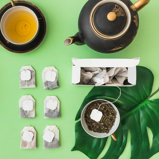 Free photo row of different tea bags with tea cup and teapot on pale green backdrop