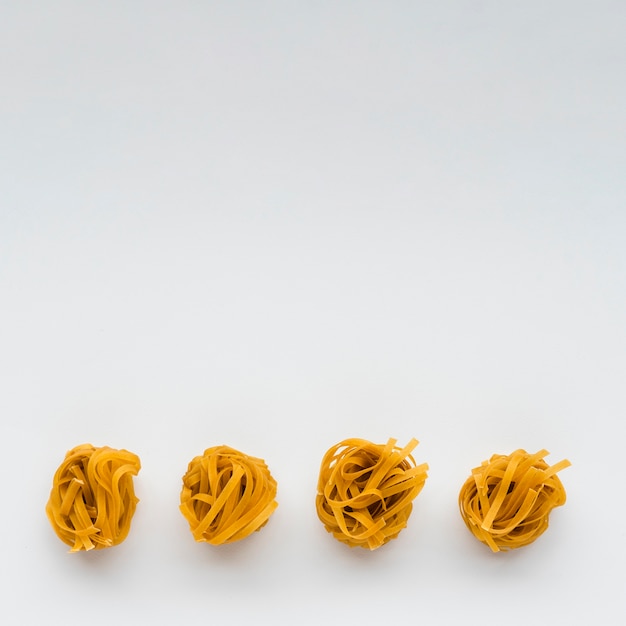 Free photo row of uncooked tagliatelle pasta at the bottom of white background