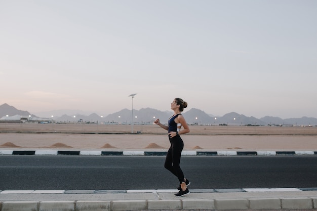 Free photo running, workout on road in early morning of joyful beautiful woman. training of strong sportswoman, energy, motivation, healthy lifestyle, cheerful mood.