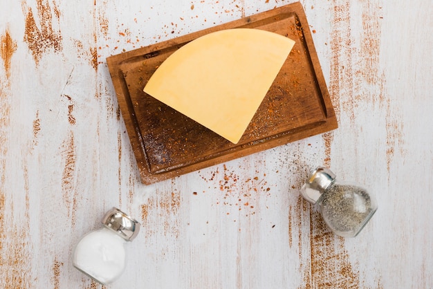 Free photo salt and black pepper shaker bottles with cheese on chopping board