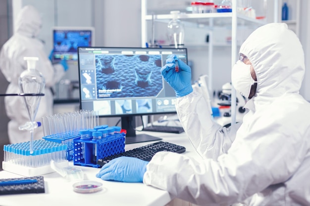 Free photo scientist in protection suit holding sample of infected blood with coronavirus in test tube