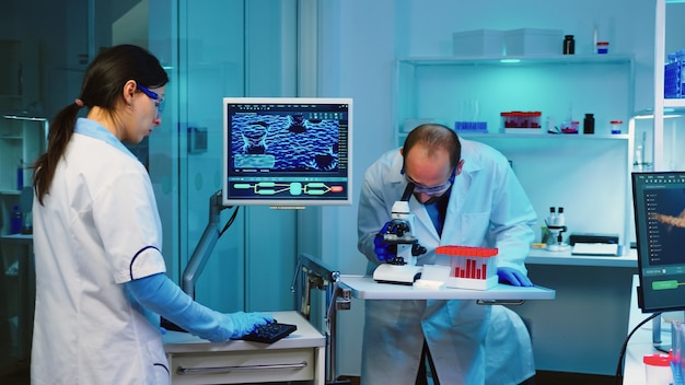 Free photo scientist researcher using microscope in laboratory while nurse taking notes on computer working overtime