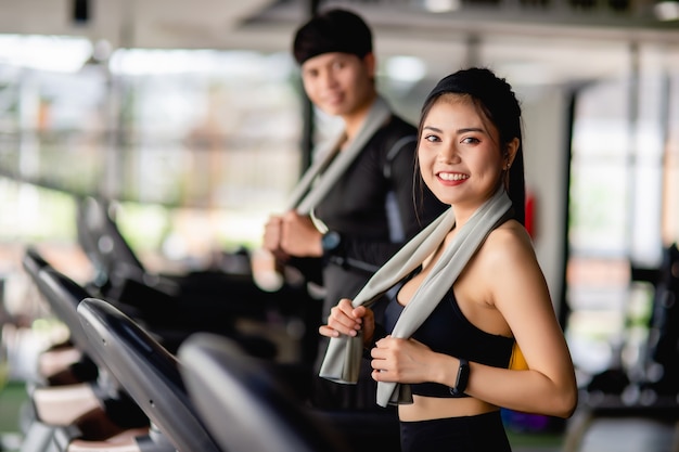 Free photo selective focus, portrait sexy woman in sportswear, running on treadmill, blurred handsome man run nearly, they are workout in modern fitness gym, smile , copy space