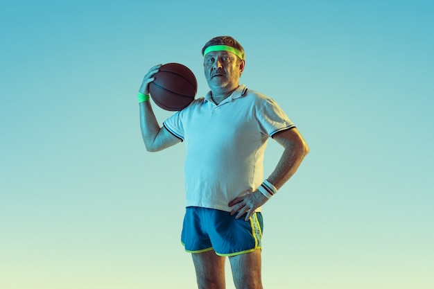 Senior man playing basketball on gradient wall in neon light