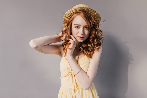 Free photo serious ginger woman in trendy summer outfit dancing on gray wall. portrait of amazing girl with wavy hairstyle posing in yellow attire.