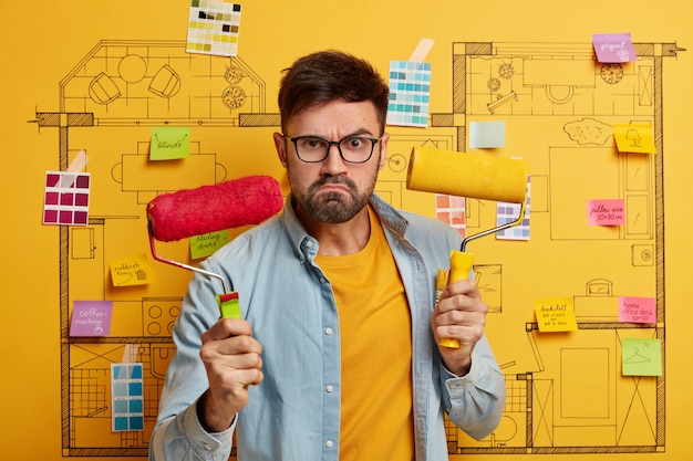 Free photo serious young male stands next to house design sketch ready for renovation