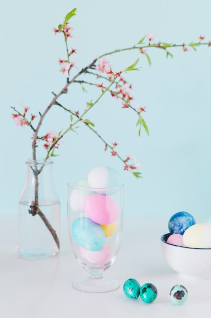 Free Photo set of bright easter eggs near flower twig in vase with water and bowl