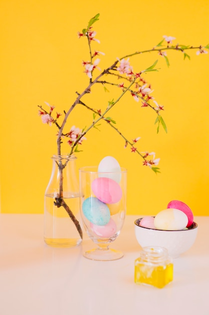 Free Photo set of bright easter eggs near flower twig in vase with water and dye liquid