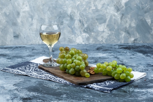 Free photo set of kitchen towel, glass of whisky and white grapes on a cutting board on a dark and light blue marble background. close-up.