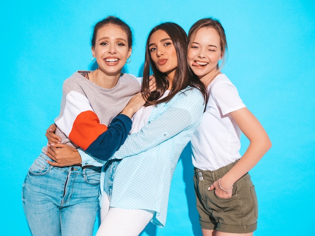 Free photo sexy carefree women posing near blue wall in studio. positive models having fun and hugging