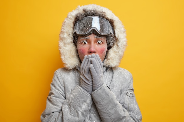 Free photo shocked stressed young woman covers mouth with hands wears hooded jacket and gloves covered with hoarfrost feels cold during seasonal outdoor activities in scandinavia.