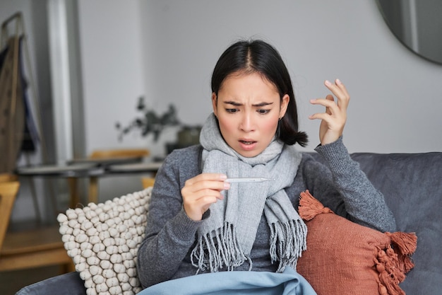 Free Photo shocked woman looks concerned at her thermometer catching cold has fever sitting on sick leave at ho