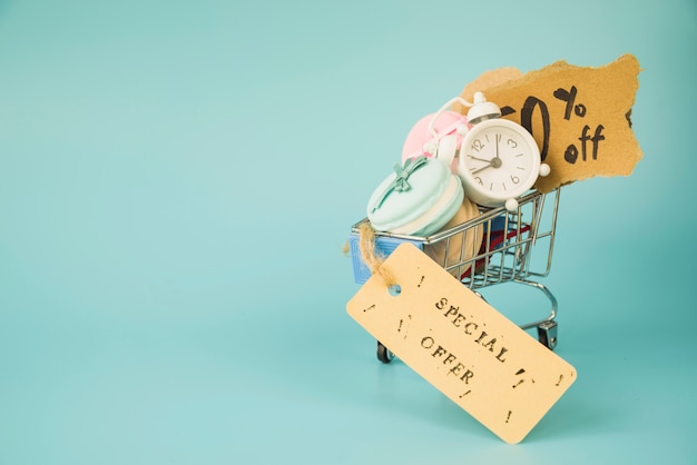 Free photo shopping trolley with alarm clock, bits of paper and macaroons near sale tag