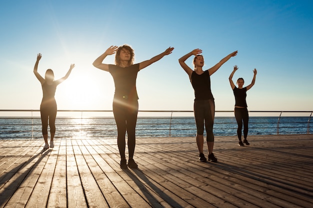 Free photo silhouettes of sportive women dancing zumba near sea at sunrise