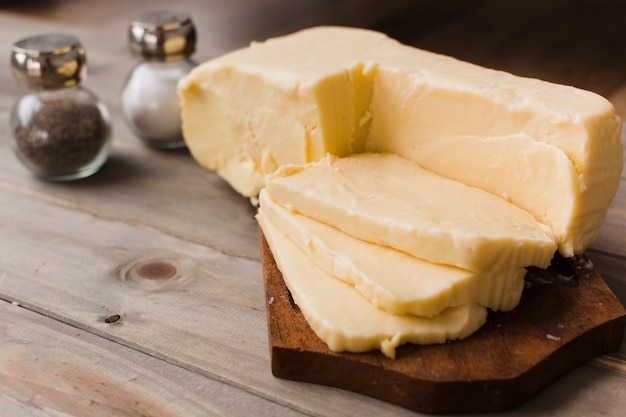 Free photo slices of cheddar cheese on chopping board with slat and pepper shaker on table