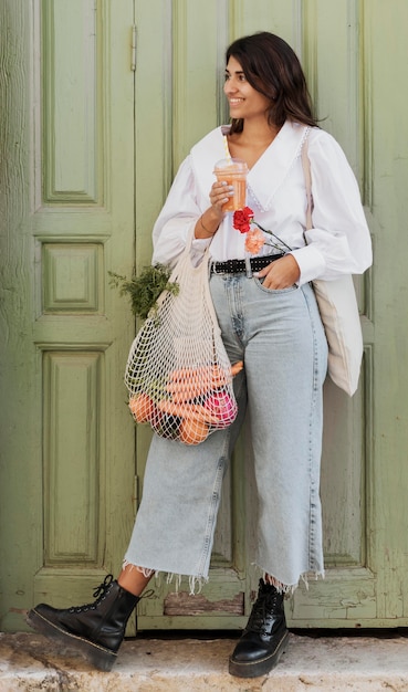 Smiley woman with grocery bags having soda outdoors