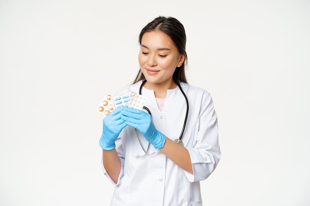 Free Photo smiling asian doctor showing medical pills advertising vitamins holding drugs with sterile gloves we...