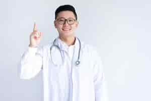 Free photo smiling asian male doctor pointing upwards