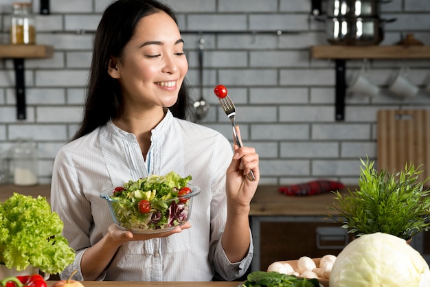 Foto gratuita donna asiatica sorridente con insalata sana in cucina