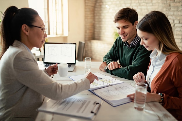 Free Photo smiling couple and insurance agent going through real estate plans during a meeting in the office focus is on man