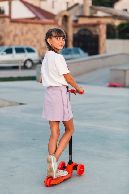 Free photo smiling girl standing on push scooter looking back