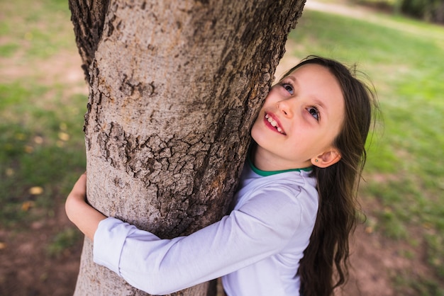 Free photo smiling little girl hugging tree in garden
