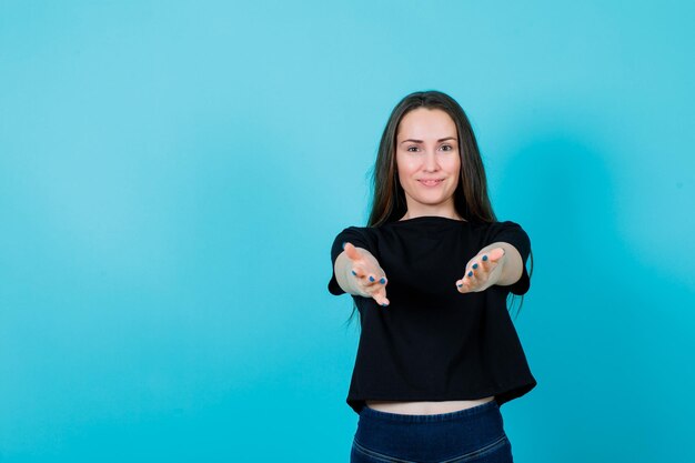 Smiling young girl is extending hands to camera on blue background