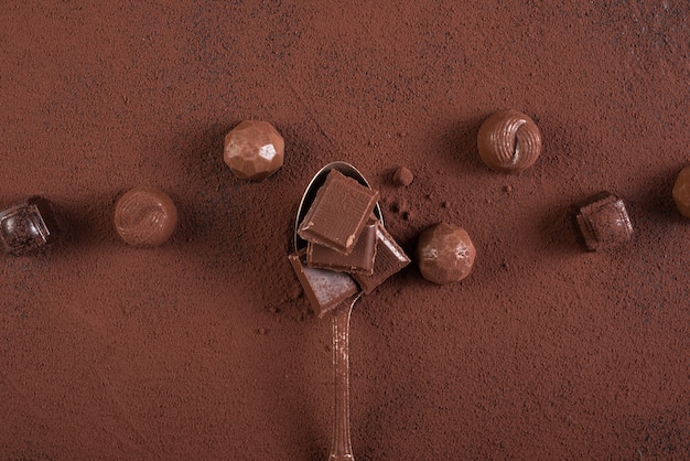 Foto gratuita cucchiaio con barrette di cioccolato quadrati caramelle e cacao in polvere