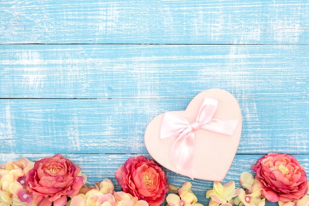 Spring background with flowers and a heart shaped gift box on a blue background