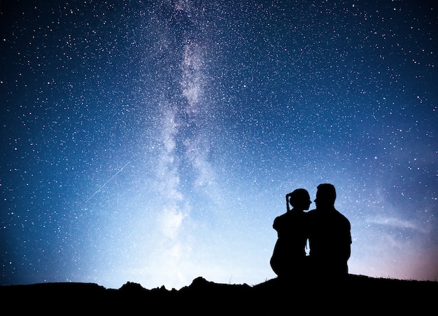 Free photo standing man and woman on the mountain with star light. hugging couple against purple milky way.