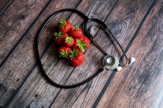 Free photo stethoscope with strawberries on top of wooden table. medical and healthcare conceptual.