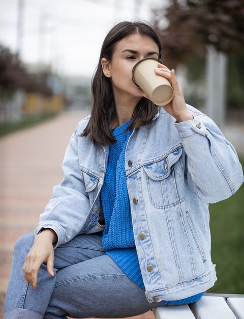 Stylish cheerful girl in casual style enjoys takeaway coffee on a walk.