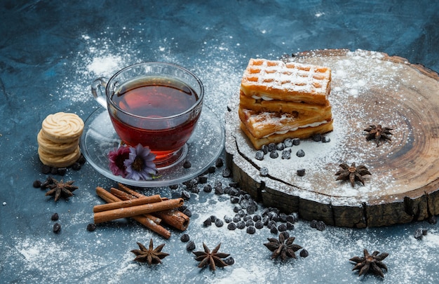 Free photo tea in a cup with waffle, biscuits, choco chips, spices high angle view on blue grunge and wooden board