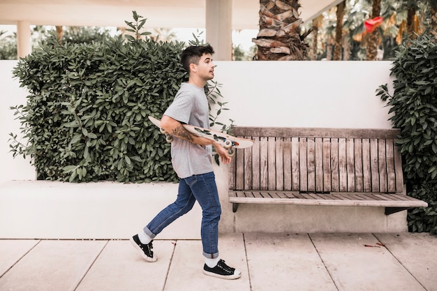 Free Photo teenage boy walking with skateboard in the park