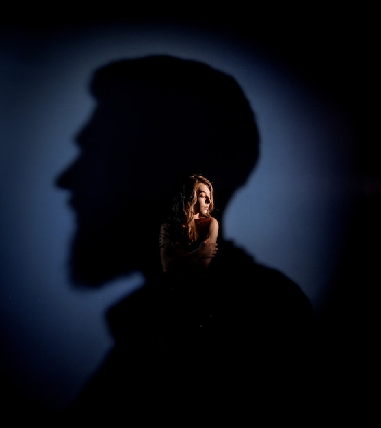 Tender caucasian blonde girl with closed eyes is standing in the man's head shadow  on the blue wall