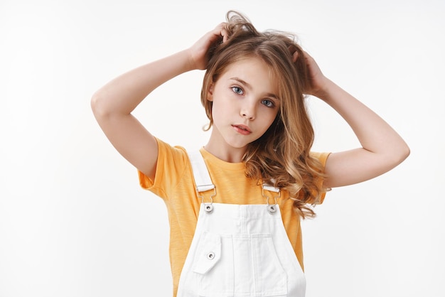 Free photo tender lovely young blond girl in summer dungarees over yellow t-shirt, look thoughtful and cute camera, scratch hair bothered, touch hairstyle, suffer head lice