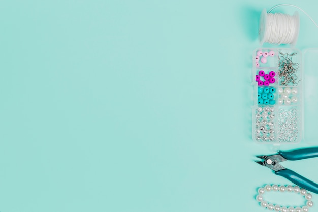 Thread spool; pearls case; plier and bracelet on teal backdrop with copy space for writing the text