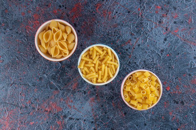 Free photo three colorful plates with different types of uncooked pasta on a dark background .