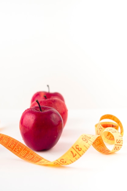 Free Photo three red apples with measuring tape on table