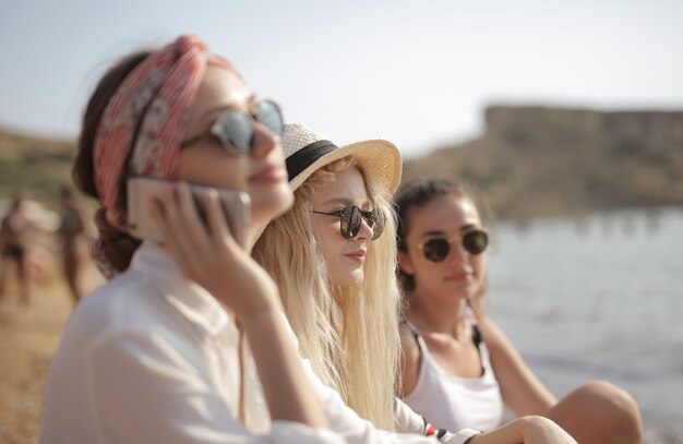 three young women with glasses at the beach, one talking on the phone