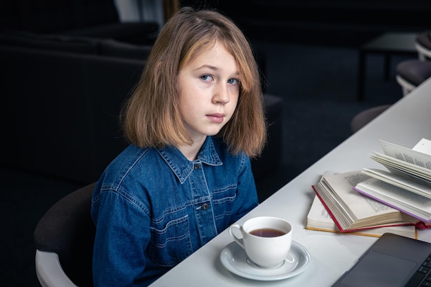 Free photo a tired girl in front of a laptop with a cup of tea and books