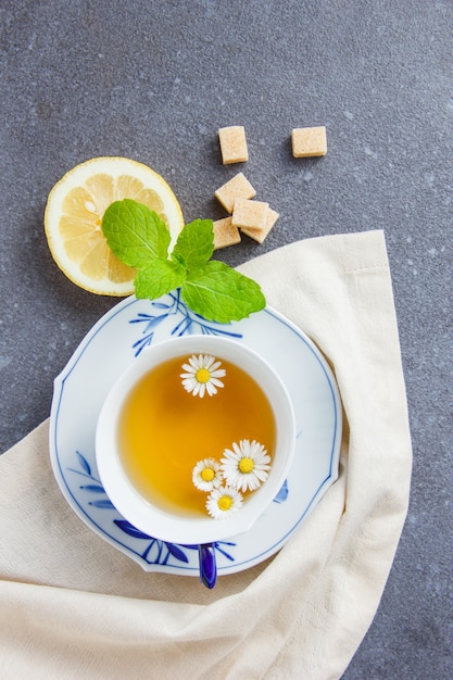 Free photo top view a cup of chamomile tea with sugar, leaves, lemon on cloth