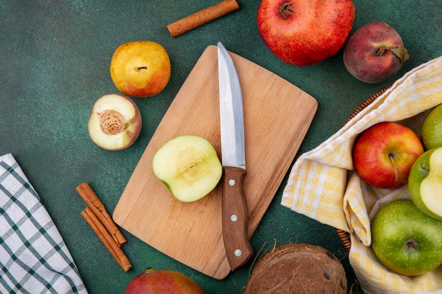 Free photo top view of fresh fruits like apple on wood kitchen board with knife peach pomegranate pear and cinnamon sticks on green